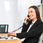 empresaria-joven-que-sonrie-mientras-que-habla-en-el-telefono-en-la-oficina